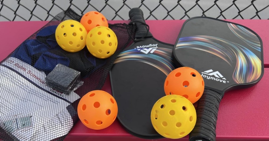 pickleball paddles, balls and carry bag on a bench by a court