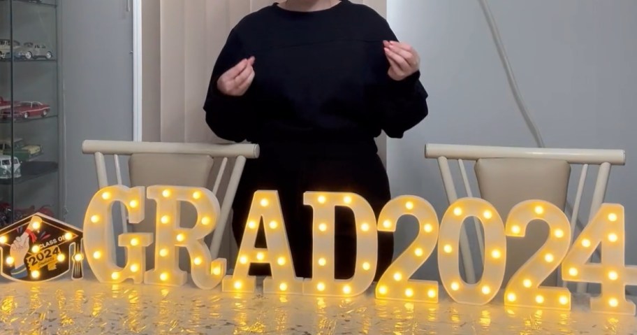 woman standing behind 2024 grad light up marquee letters that are set up on a table