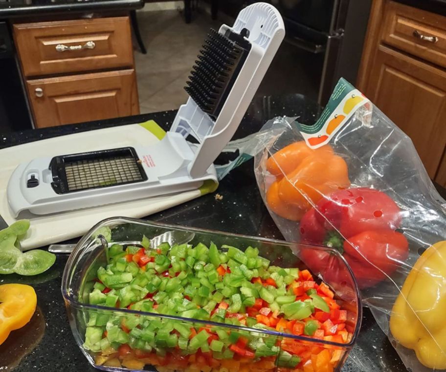 veggie slicer on a kitchen island next to the slicer container shown with multi colored bell peppers