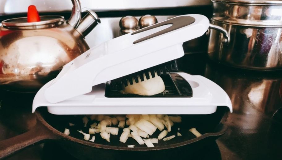 a veggie slicer over an iron skillet loaded with white onion