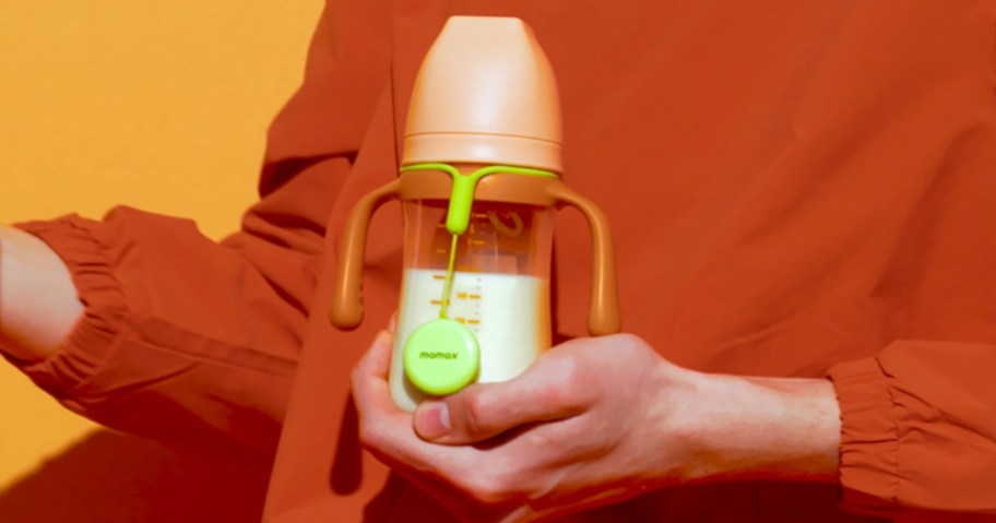 hand holding a baby bottle with a yellow Momax tracker tag with strap attached