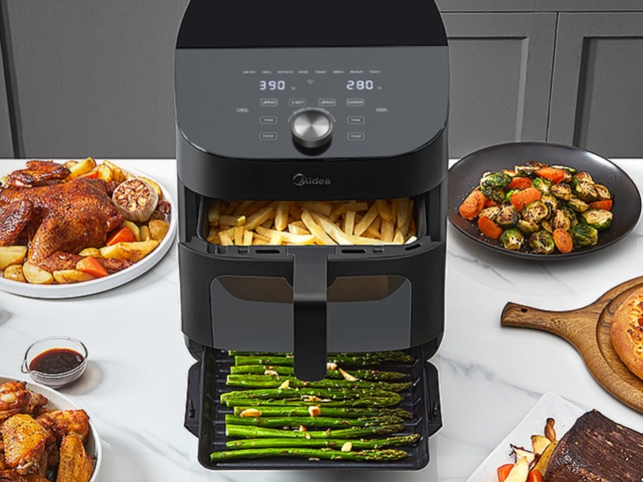 black air fryer with basket of fries and baking pan with asparagas open