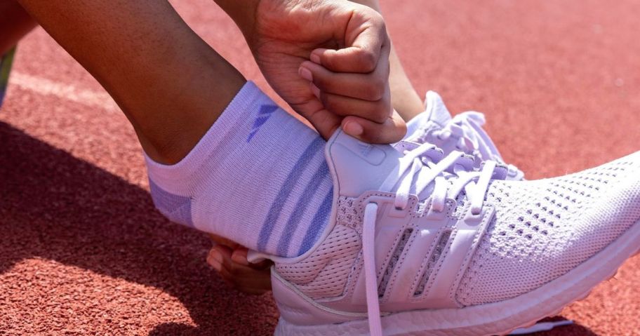 Girl sliding their foot into an Adidas Shoe wearing Adidas socks