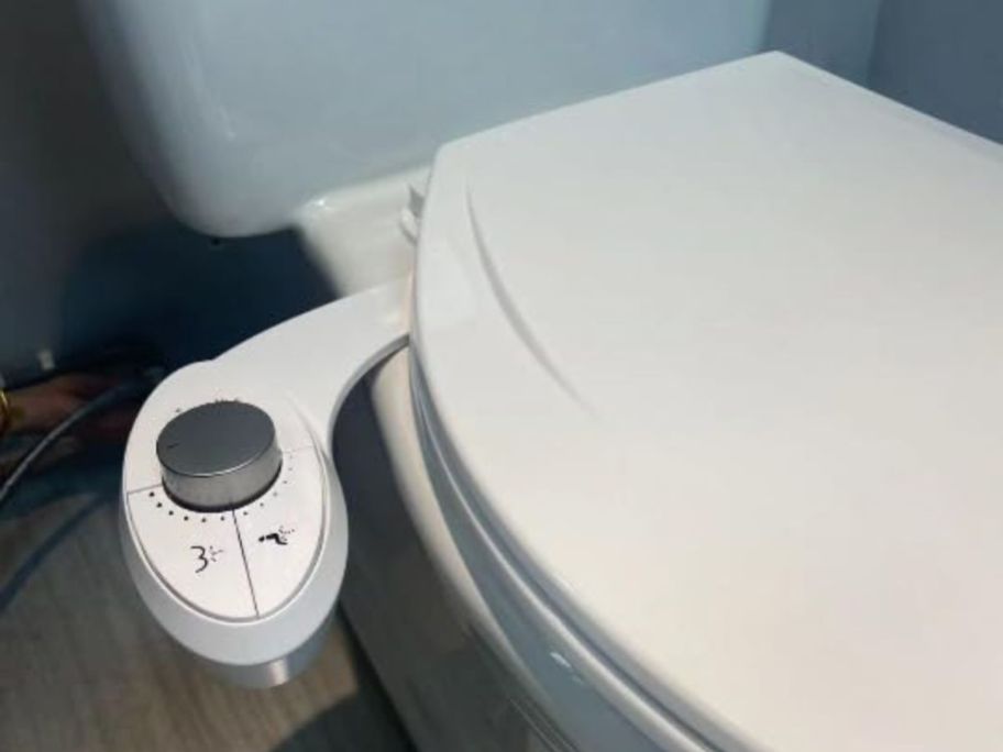 white toilet closed showing slim bidet attachment on it