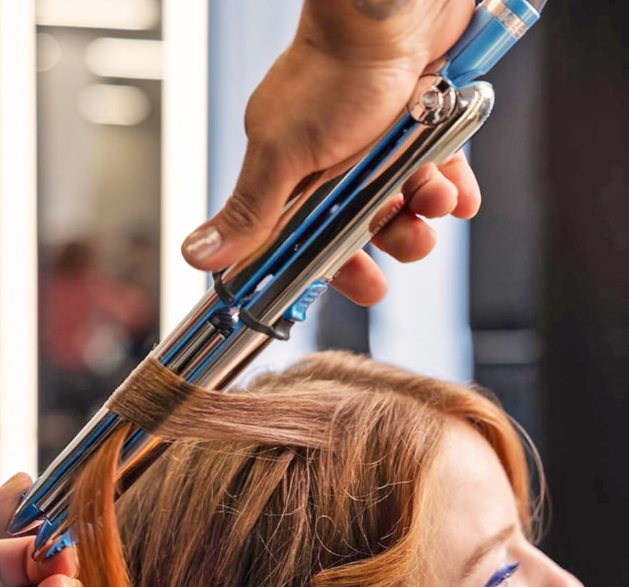 stylist using hair straightener to curl hair