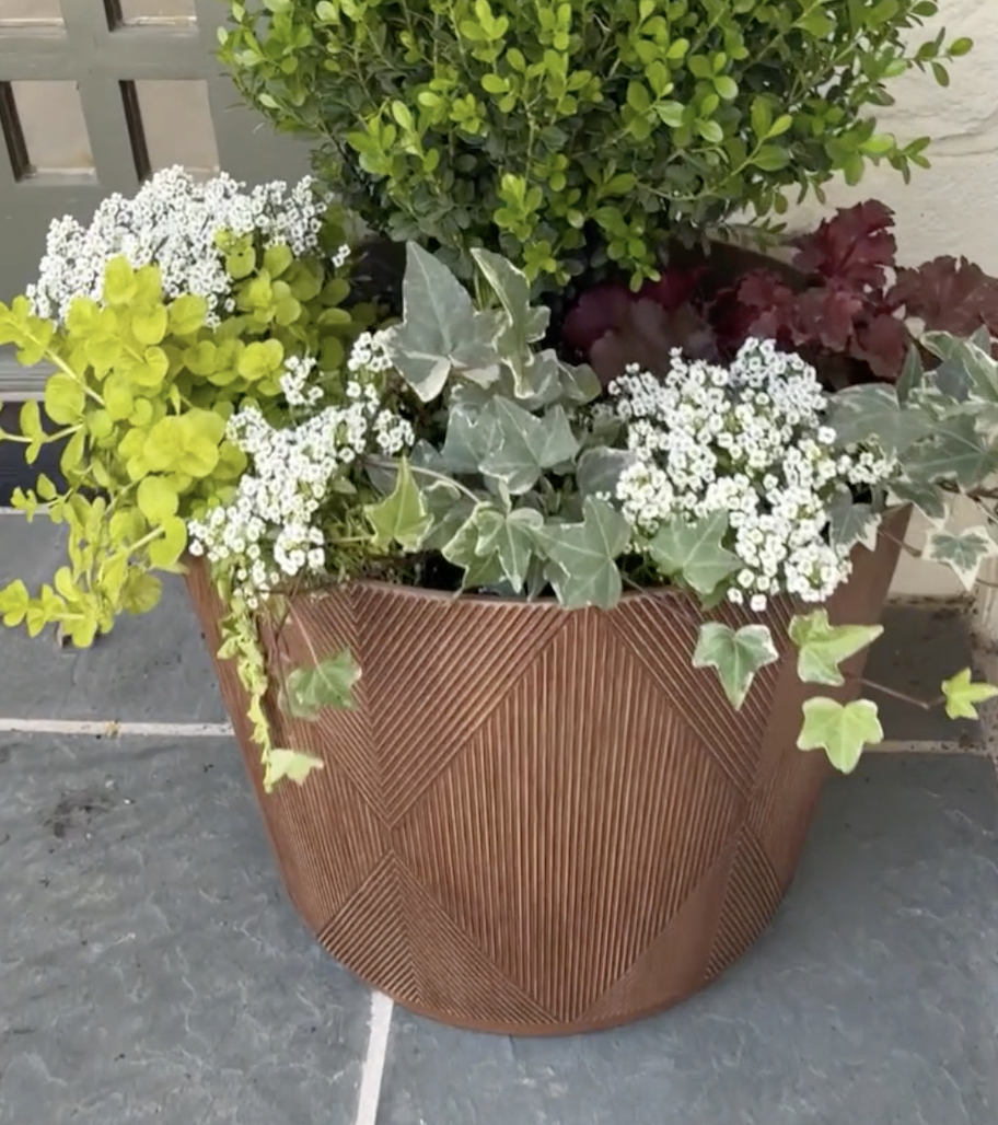 close up of large brown planter with flowers insides on slate tile patio