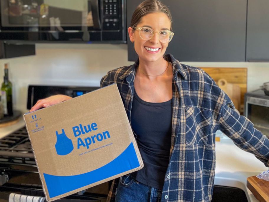 woman carrying a blue apron meal box in her kitchen