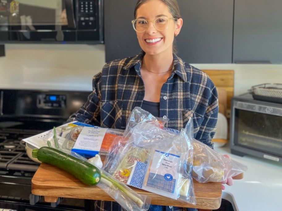 woman holding a cutting board filled with blue apron pre-portioned ingredients