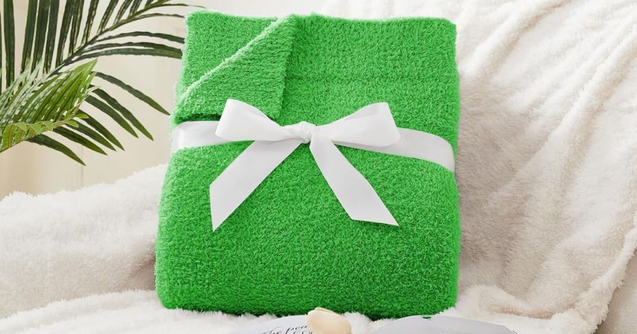 a green throw blanket folded and tied with a ribbon propped up on a white sofa