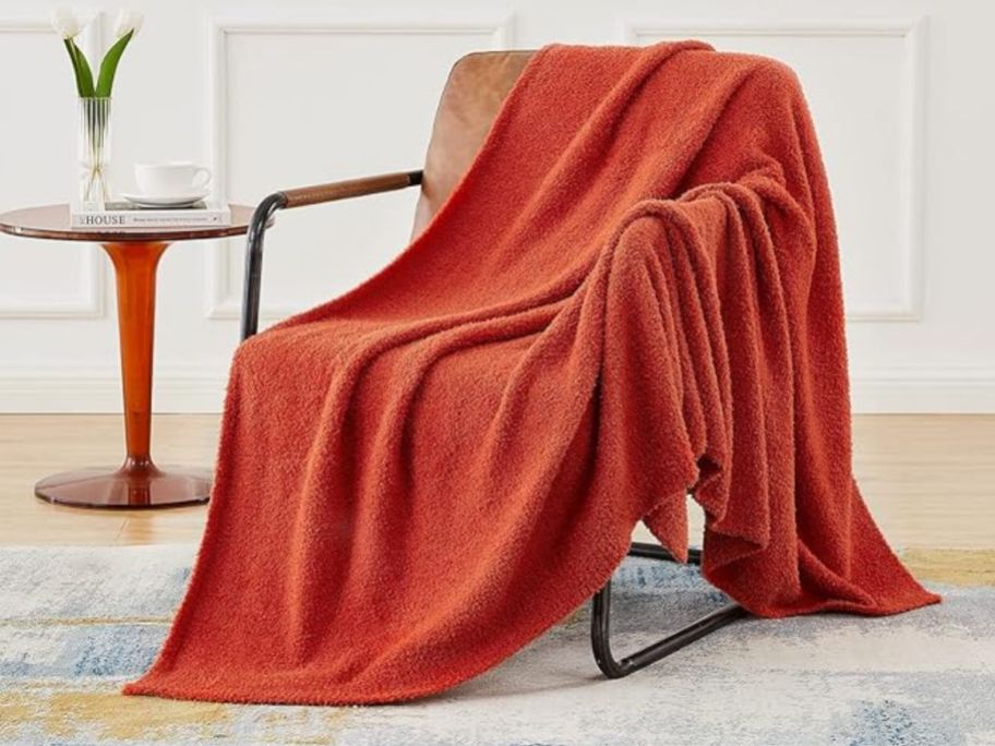 an orange throw blanket draped over the back of a beige accent chair