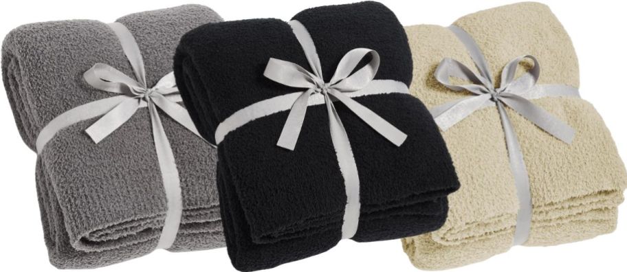 three throw blankets in gray,, black and beige folded and tied with a ribbon on a white background