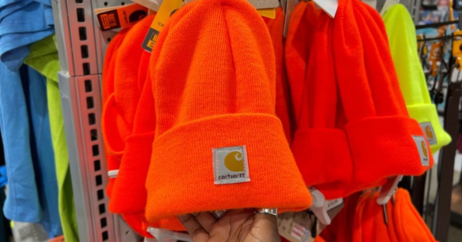 Hand touching a bright orange Carhartt beanie hanging on a display at a Carhartt Store