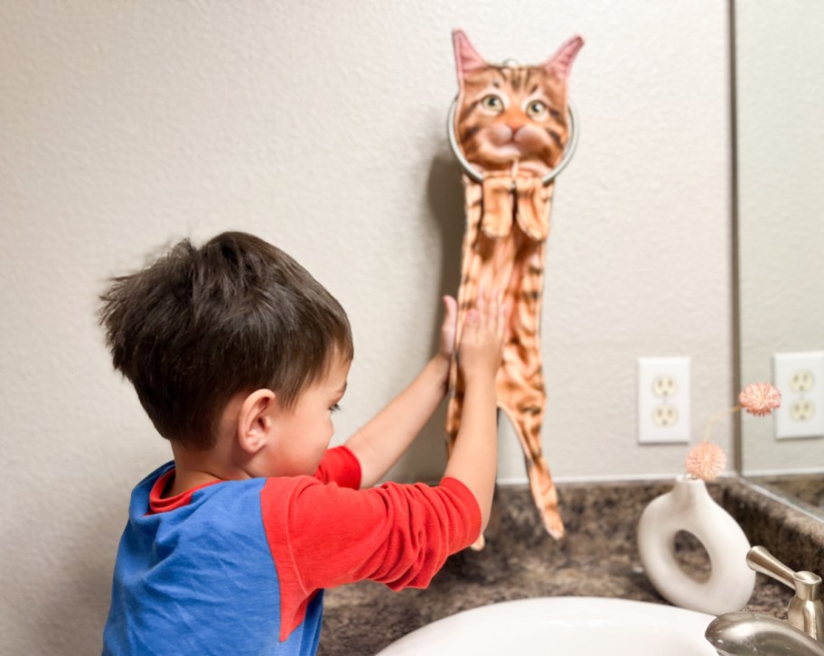 Boy drying his hands on a funny cat hand towel hanging in the bathroom