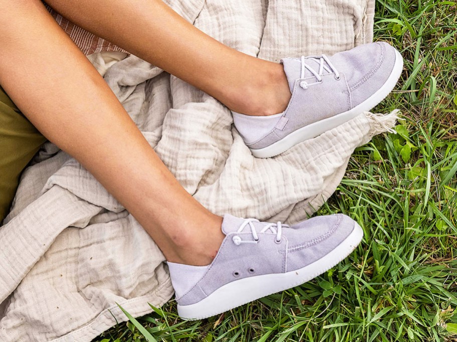 woman laying in grass wearing grey sneakers