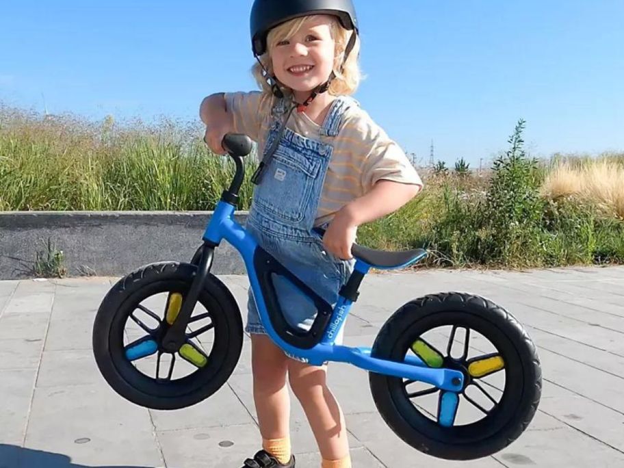 kid wearing helmet lifting up blue balanace bike