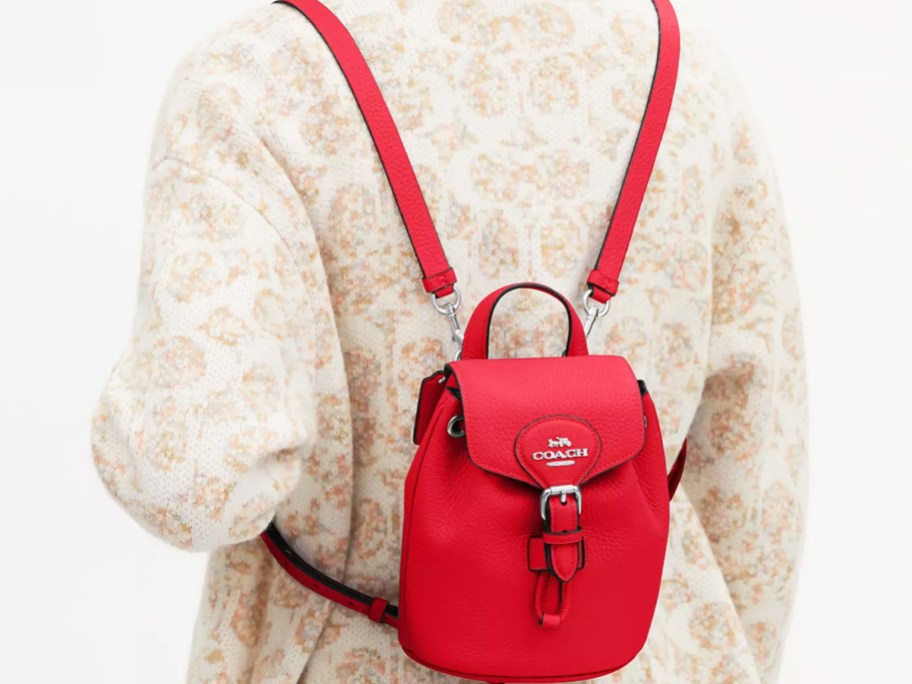 a model wearing a mini red convertible backpack on her back 