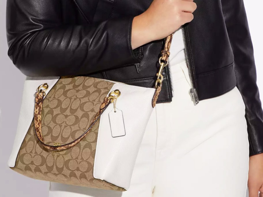 woman in black leather jacket with white jeans and coach crossbody bag