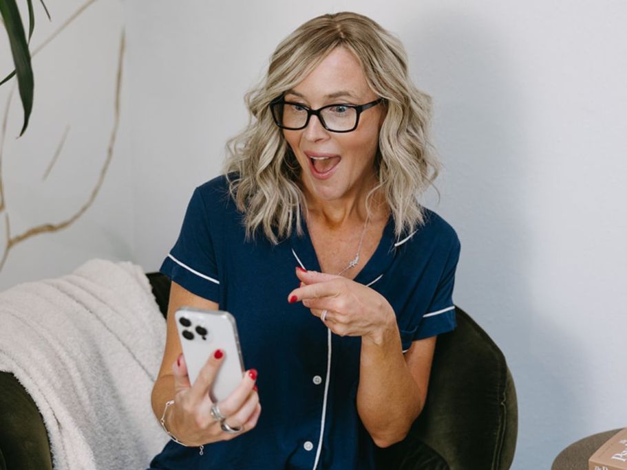 Woman holding up cell phone with one hand and pointing at the screen with her other hand