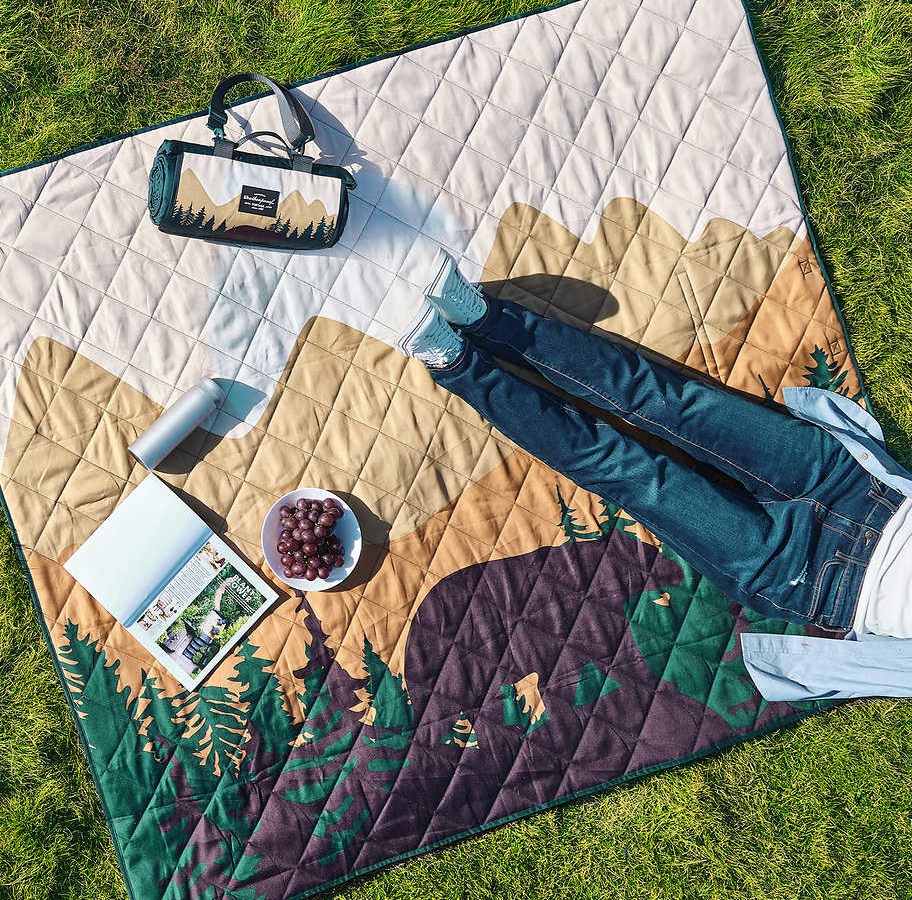 Woman laying outdoors on a blanket with a mountain print