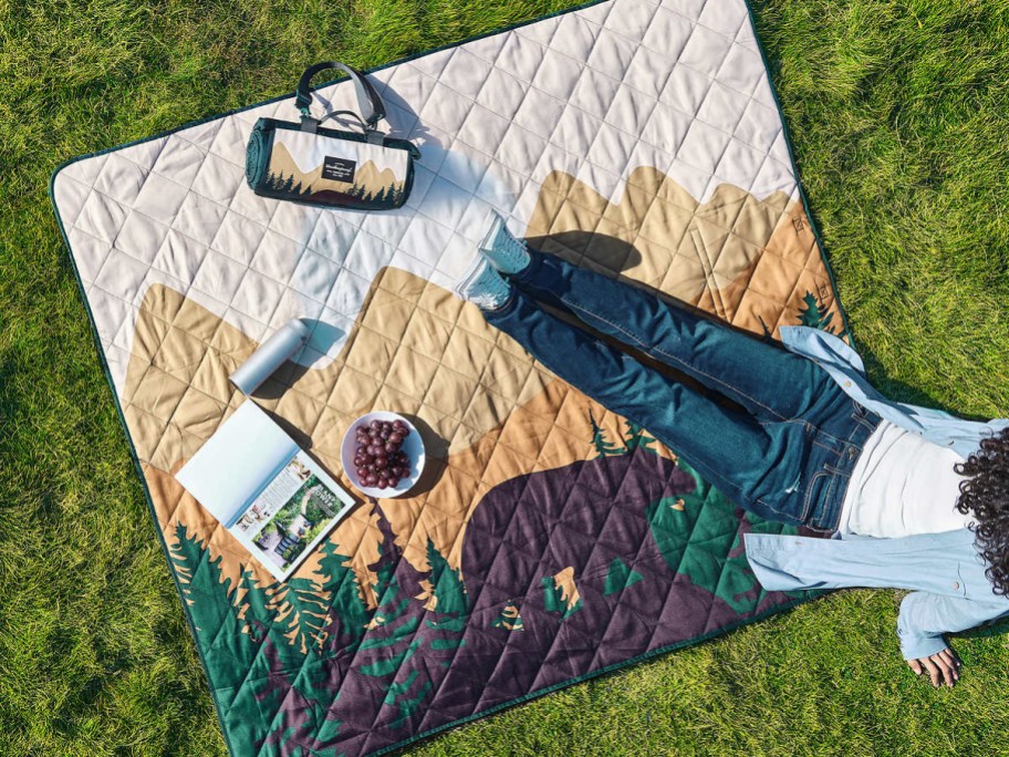 Woman laying outdoors on a blanket with a mountain print 