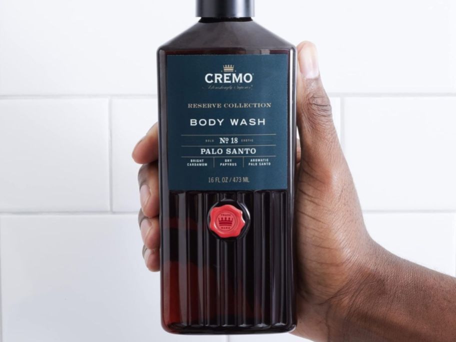 A hand holding a bottle of Cremo Body Wash Palo Santo