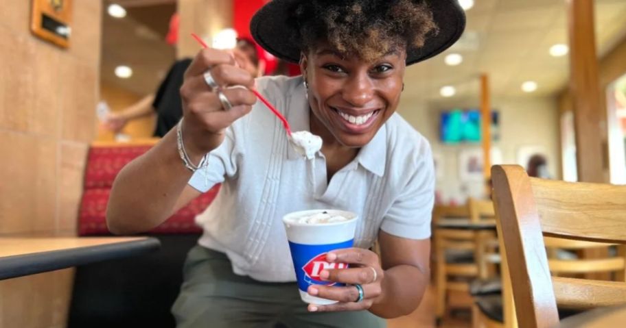 a smiling woman holding a dairy queen blizzard in one hand and a red plastic spoon in the other