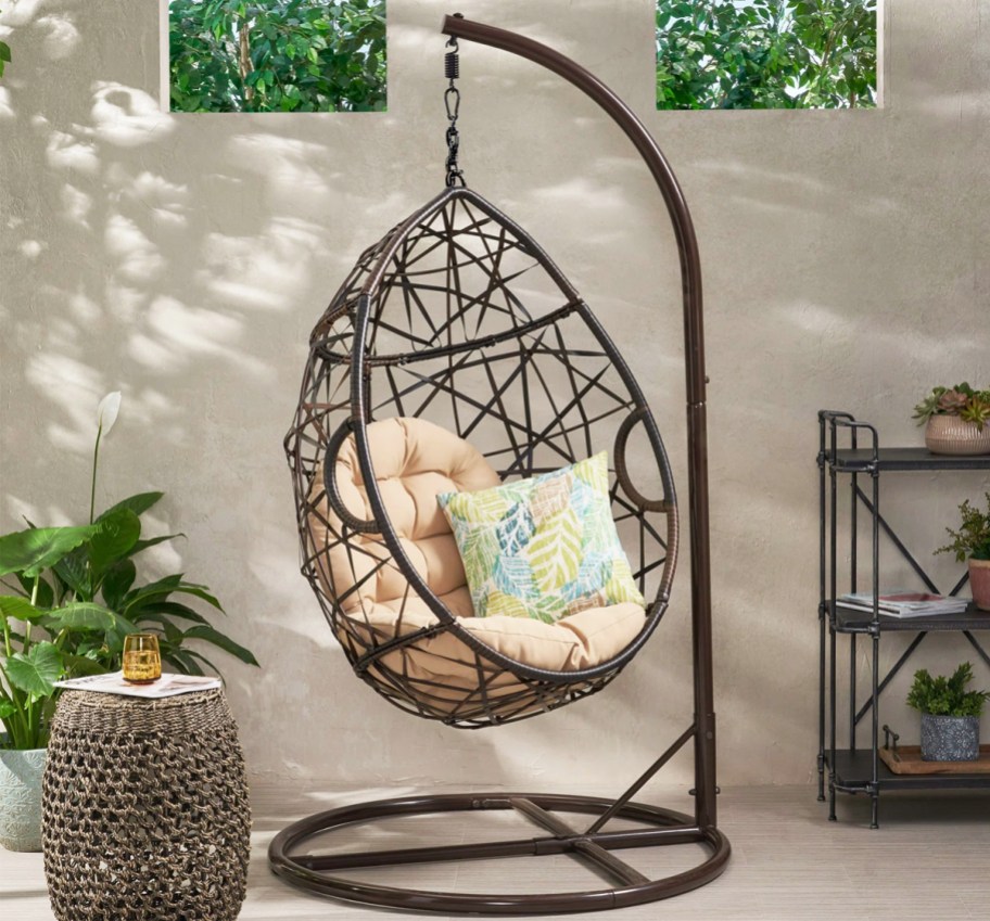 brown egg chair hanging from stand on a patio