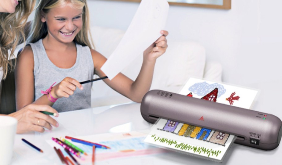 Young girl, using desktop laminator to laminate colored drawing
