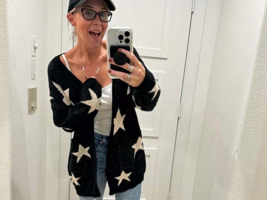 Woman taking selfie in front of mirror wearing jeans and black and white star cardigan