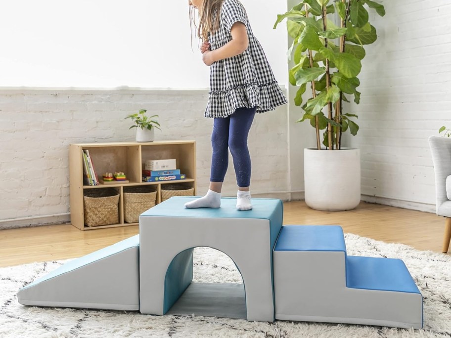 little girl playing on a grey and blue soft kids climbing playset in a living room