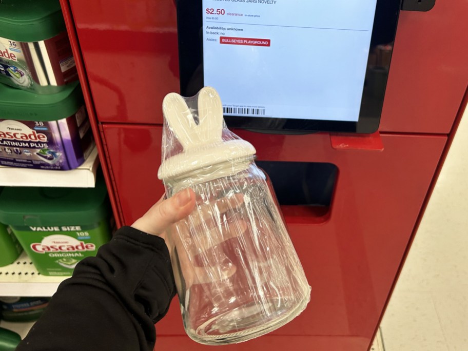 holding a glass jar with rabbit ears lid up to a price scanner