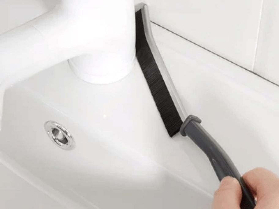 Hand using a gap cleaning brush to clean behind a sink faucet handle