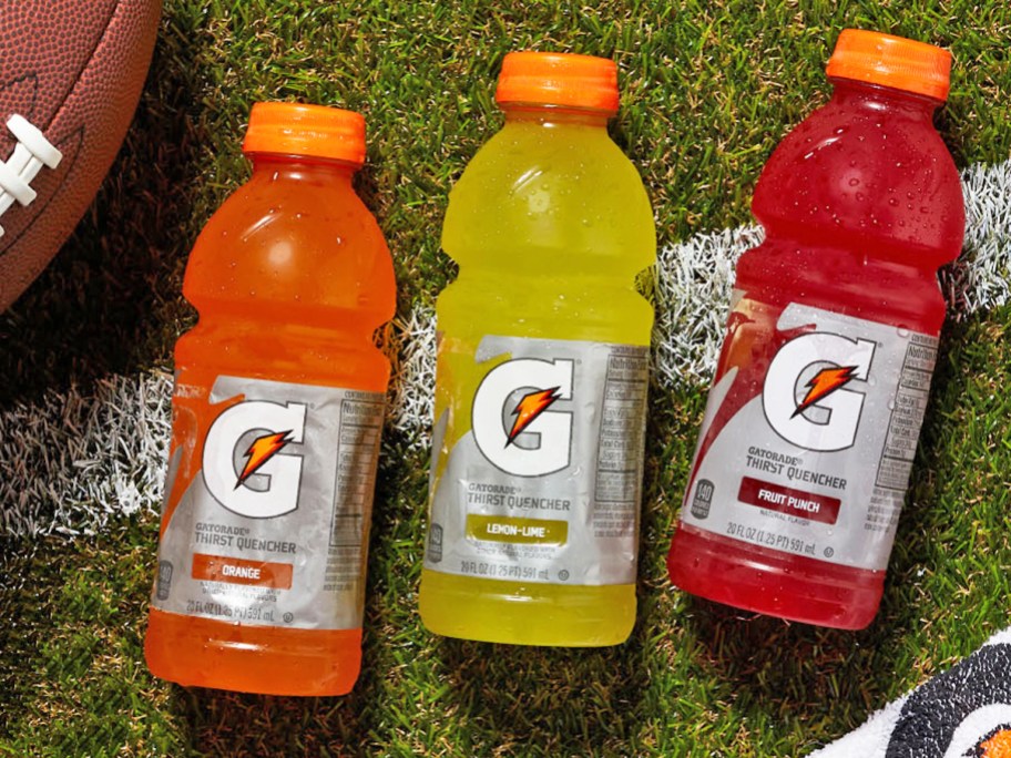 Fruit Punch, Lemon Lime, and Orange bottles of Gatorade laying in grass near football