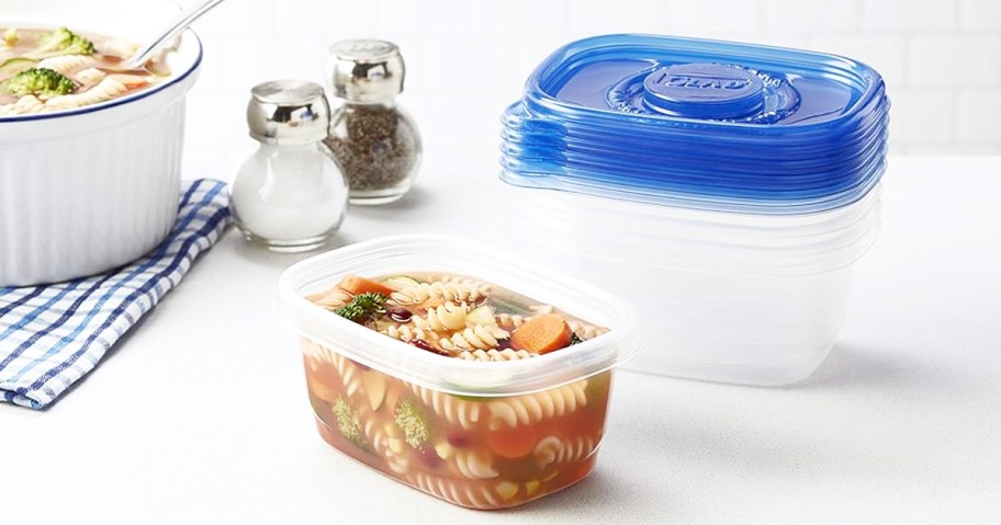 soup in a plastic food container with more containers and pot of soup behind it
