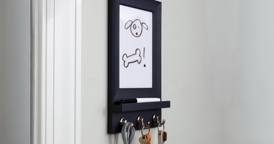 black dry erase board with key hooks on a wall with a dog and bone drawn on it