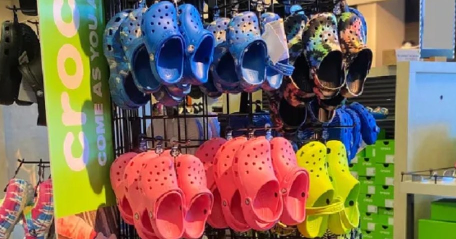 various colors of Crocs clogs on a display in store next to a Crocs sign