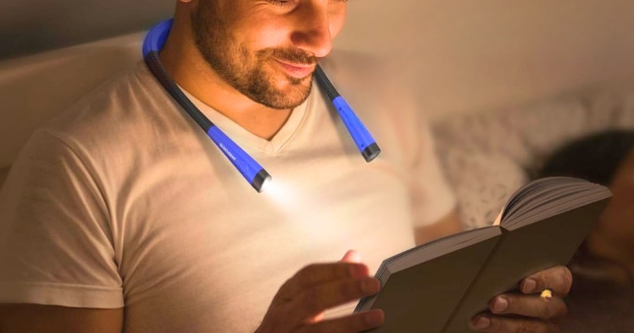 man wearing a blue led neck reading light reading a book sitting in bed
