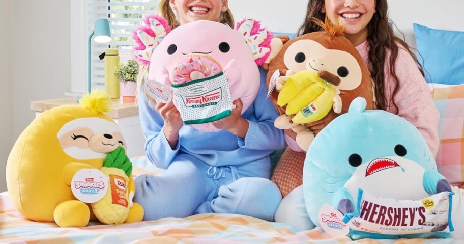 2 girls holding Snackles plushes with more Snackles beside