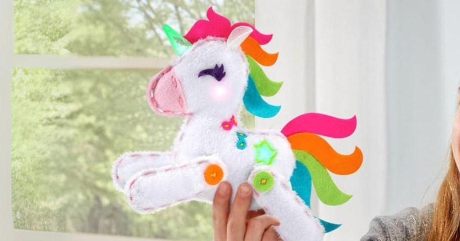 child's hand holding a white toy Unicorn with multicolor hair and accents