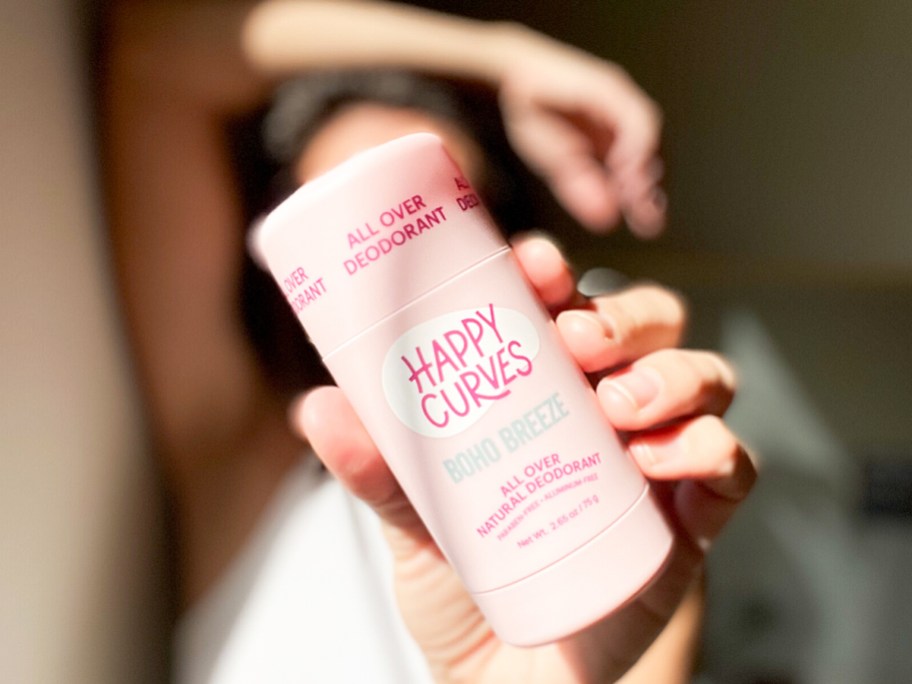 woman holding up a pink stick of happy curves deodorant