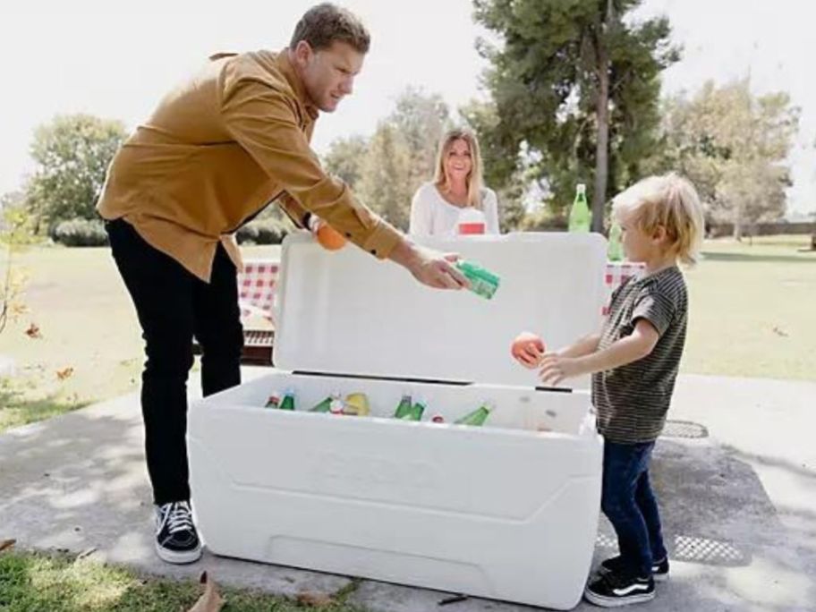 Man handing a child a beverage from a large igloo cooler