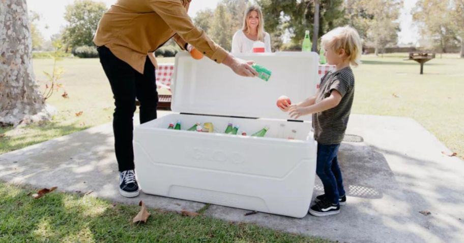 A man giving a drink to a boy from an Igloo cooler