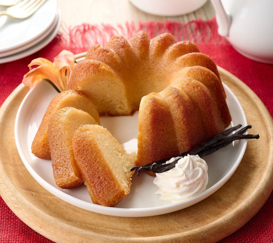 a yellow bundt shaped cake with 3 slices cut from it arranged on the same plate, along side heavy cream with vanilla beans