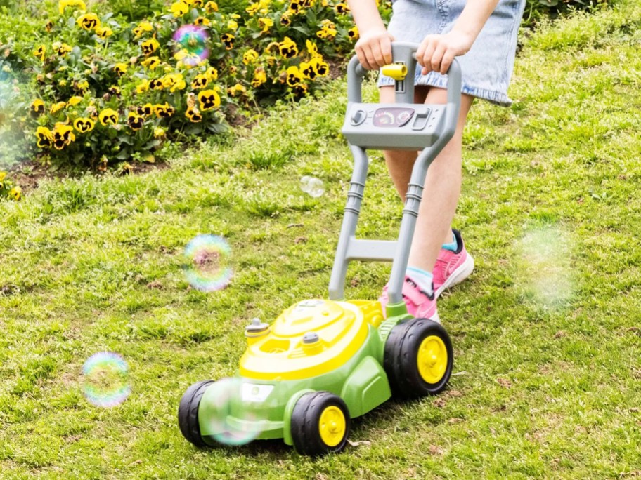 girl pushing a yellow and green bubble mower on grass