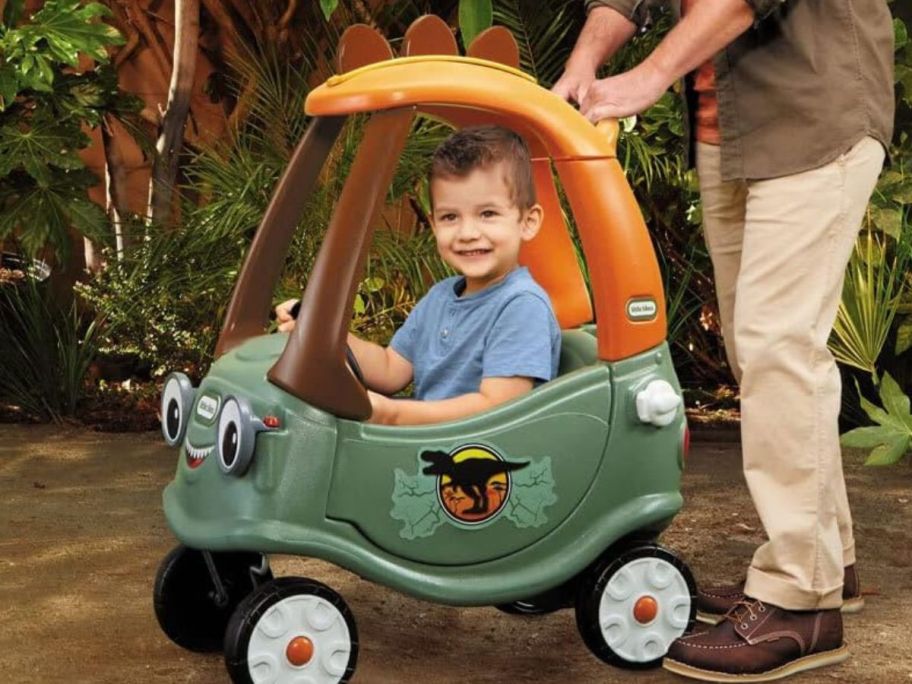 Little boy riding in a Little Tikes Dino Cozy Coupe while being pushed by his father