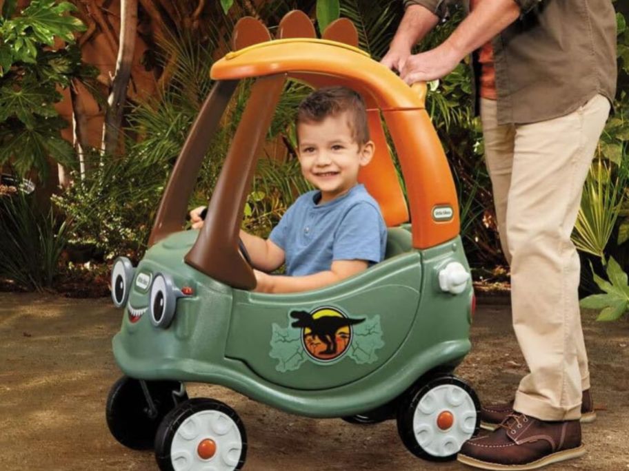 Little boy riding in a Little Tikes Dino Cozy Coupe while being pushed by his father