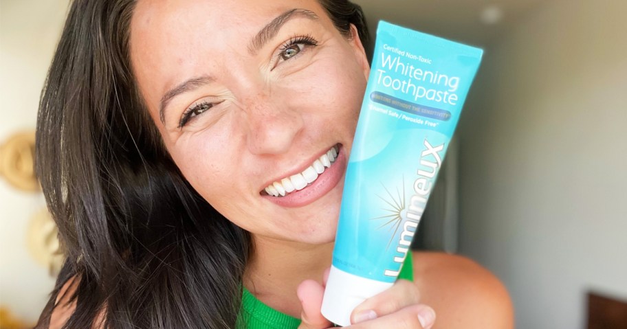 woman smiling and holding tube of Lumineux Whitening Toothpaste near her mouth