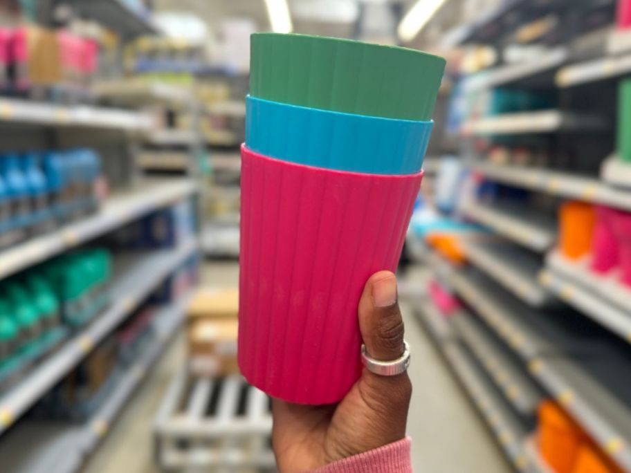 a womans hand holding a stack of 3 tumblers in green, blue and fuchsia