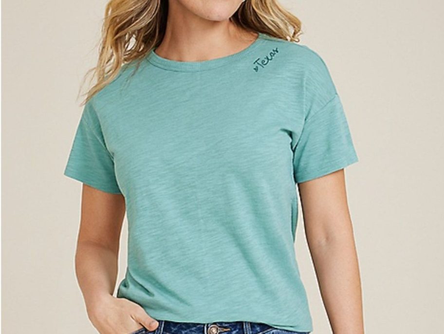 Woman wearing a teal tee with Texas embroidered below the neckline 