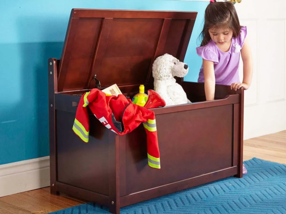 girl reaching into large brown toy chest